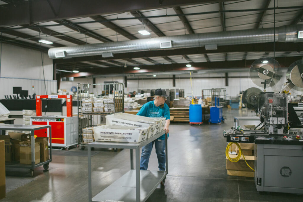 Tippy Fox moves mail trays in the production area of Trevett's Print + Mail.